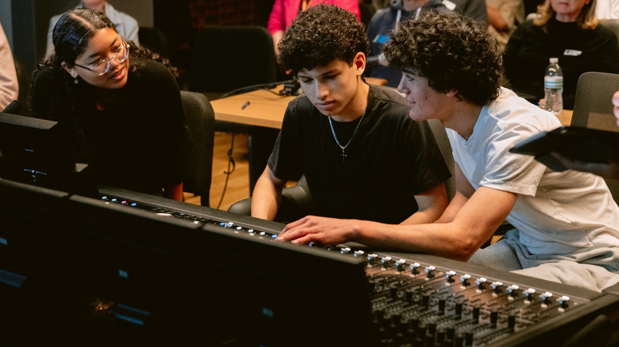 young people sit and look at a sound board in a recording studio