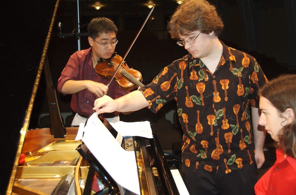 A violinist and pianist and composer look at sheet music.