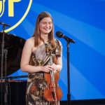 girl holding violin stands at microphone