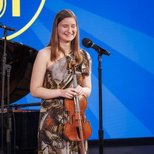 Girl with violin stands in front of microphone