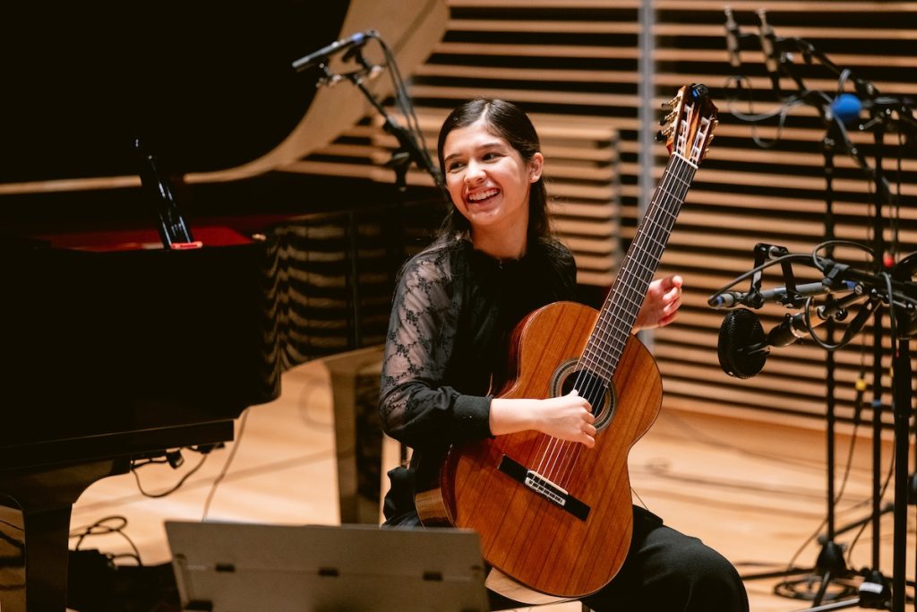 girl with guitar smiles over her shoulder in a recording studio