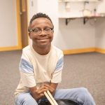 boy sits with drum sticks.